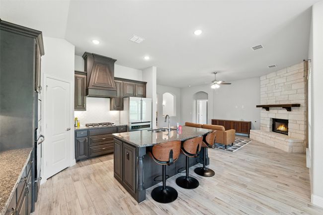 Kitchen featuring ceiling fan, a stone fireplace, arched walkways, a kitchen bar, and stone countertops | Image 14