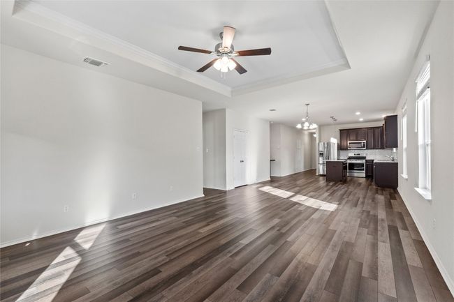 Unfurnished living room featuring plenty of natural light, ceiling fan with notable chandelier, laminate / wood-style floors, and a tray ceiling | Image 20
