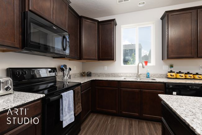 Kitchen featuring black appliances, a sink, dark wood-style flooring, dark brown cabinetry, and light stone counters | Image 12