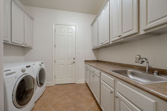 Clothes washing area featuring a sink, cabinet space, light tile patterned floors, baseboards, and washer and dryer | Image 31