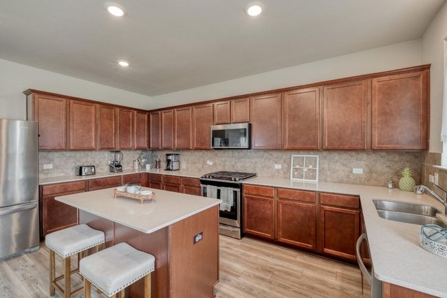 Kitchen featuring light countertops, a kitchen bar, backsplash, a sink, and appliances with stainless steel finishes | Image 16