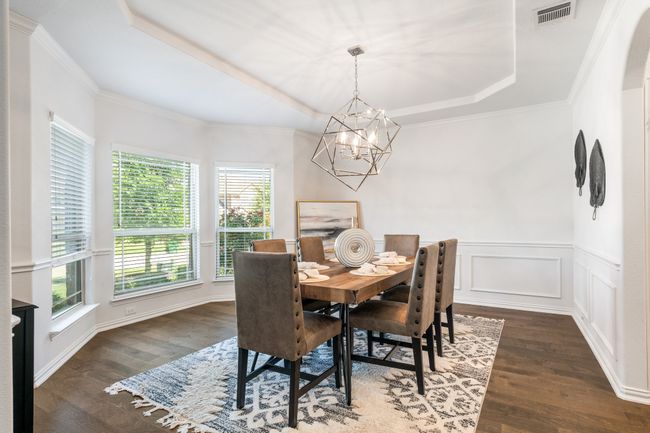 Dining space with a tray ceiling, wood finished floors, a chandelier, crown molding, and a wainscoted wall | Image 8