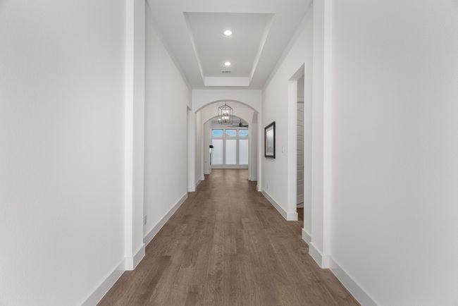 Hallway featuring wood finished floors, arched walkways, baseboards, recessed lighting, and a tray ceiling | Image 9