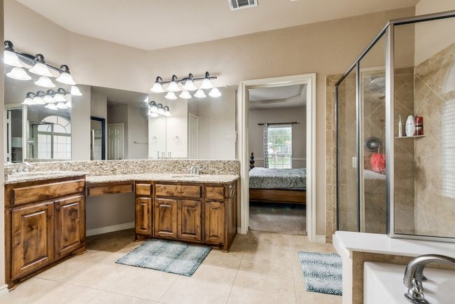 Ensuite bathroom with a stall shower, double vanity, tile patterned flooring, a garden tub, and baseboards | Image 22
