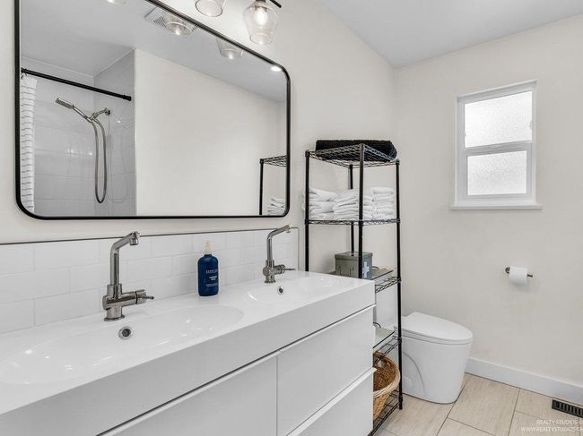 Main/upper floor bathroom, beautifully renovated with gleaming white cabinetry and double sinks, stylish mirror/lighting, modern toilet, and bathtub/shower combination plus new window. | Image 32