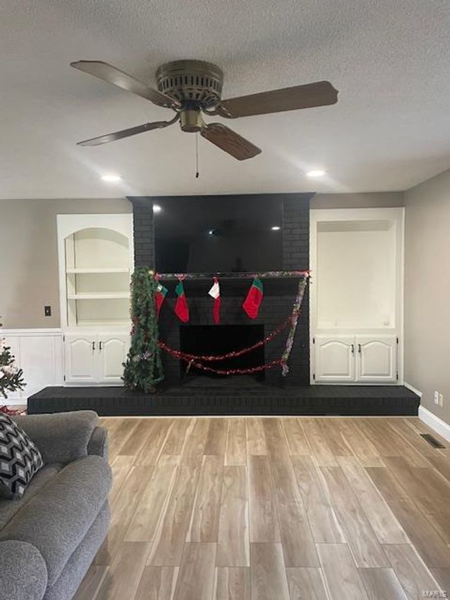Living room featuring built in shelves, a fireplace, a textured ceiling, and light hardwood / wood-style flooring | Image 15