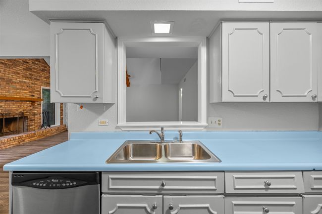 Kitchen with stainless steel dishwasher, a sink, white cabinetry, a brick fireplace, and light countertops | Image 15