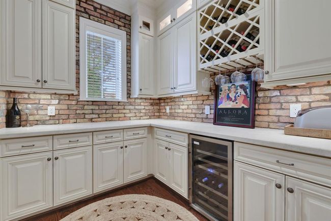 Connected to the dining room, a thoughtfully designed wine room offers both style and function. Outfitted with a built-in wine rack, wine refrigerator, and striking brick backsplash, it also features crisp white cabinetry topped with luxurious Taj Mahal quartzite countertops, creating the perfect space to display and enjoy your favorite vintages. | Image 8