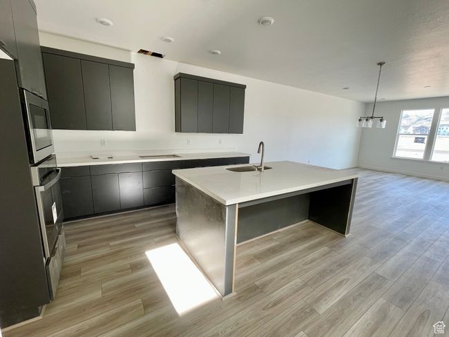 Kitchen featuring light wood-style flooring, modern cabinets, a center island with sink, appliances with stainless steel finishes, and light countertops | Image 4