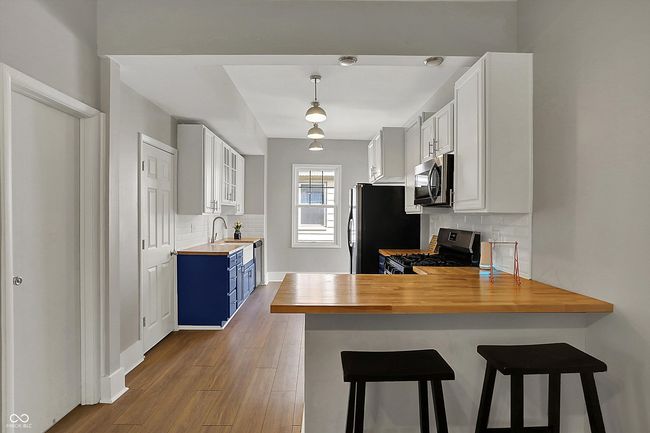 kitchen with dark wood-style floors, blue cabinets, butcher block counters, decorative backsplash, and appliances with stainless steel finishes | Image 15