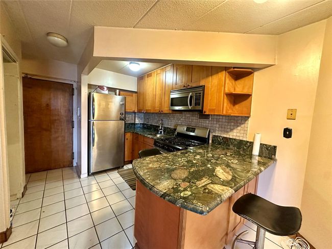 Kitchen with stainless steel appliances, a peninsula, decorative backsplash, brown cabinets, and light tile patterned flooring | Image 7