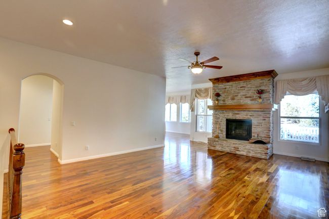 Unfurnished living room with baseboards, a fireplace, ceiling fan, arched walkways, and wood finished floors | Image 7