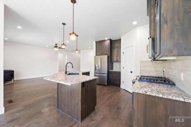 Kitchen with stainless steel fridge with ice dispenser, a wood stove, dark brown cabinetry, tasteful backsplash, and open floor plan | Image 7