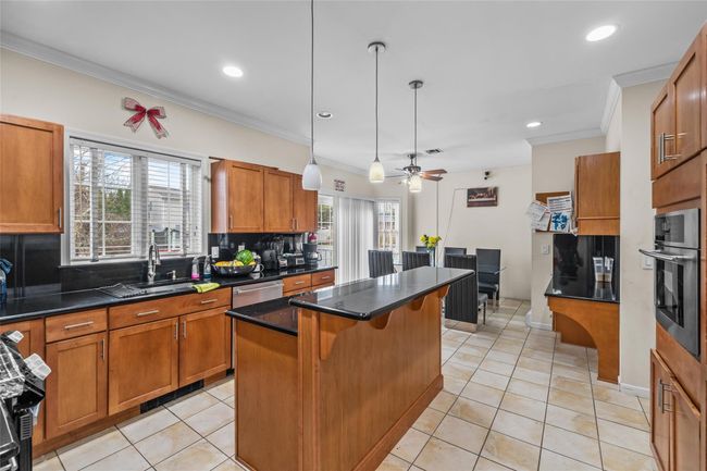 Kitchen with a breakfast bar area, brown cabinetry, decorative backsplash, stainless steel appliances, and a sink | Image 13