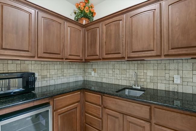 UPSTAIRS Kitchenette featuring beverage cooler, black microwave, dark stone counters, backsplash, and pecan cabinetry near the Family/Game Room. | Image 20
