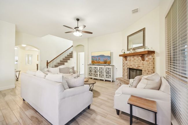 Living room with light wood-type flooring, a brick fireplace, visible vents, ceiling fan, and arched walkways | Image 8