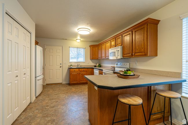 Kitchen with a breakfast bar, a textured ceiling, a peninsula, brown cabinetry, and white appliances | Image 8