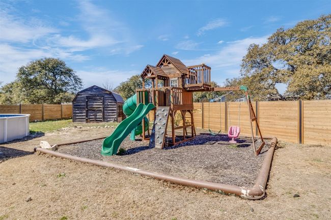 View of playground featuring a fenced in pool, an outdoor structure, and a fenced backyard | Image 25
