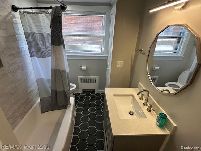 Bathroom with vanity, radiator, shower / bathtub combination with curtain, and dark tile patterned floors | Image 13