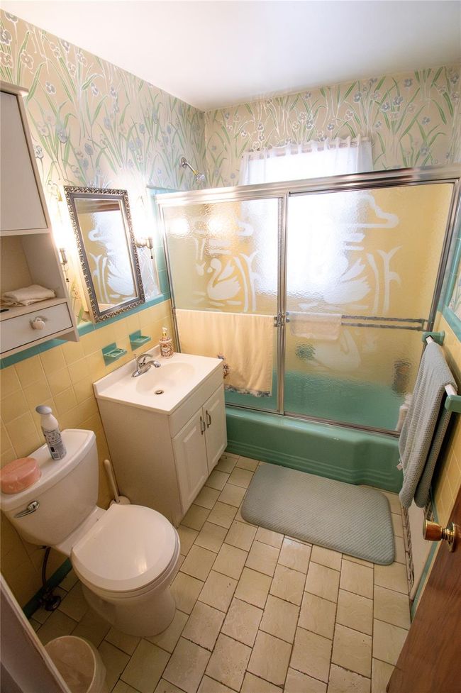 Bathroom with wallpapered walls, bath / shower combo with glass door, toilet, vanity, and tile walls | Image 10