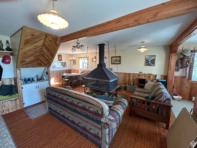 Carpeted living room with a wainscoted wall, wood walls, a chandelier, healthy amount of natural light, and a wood stove | Image 31