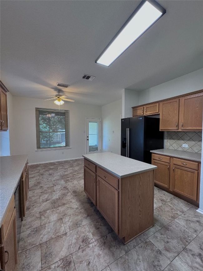 Kitchen with black fridge, a center island, a ceiling fan, brown cabinets, and light countertops | Image 9