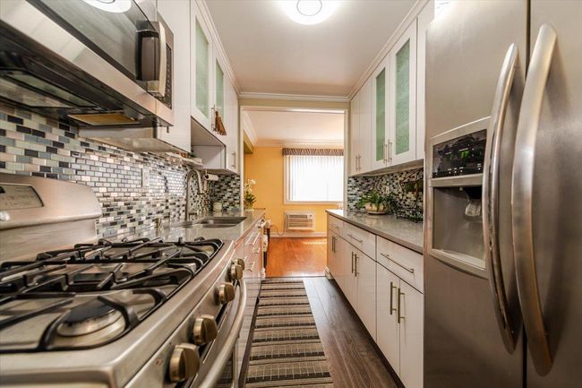 Kitchen with stainless steel appliances, ornamental molding, tasteful backsplash, dark wood-style floors, and white cabinetry | Image 10
