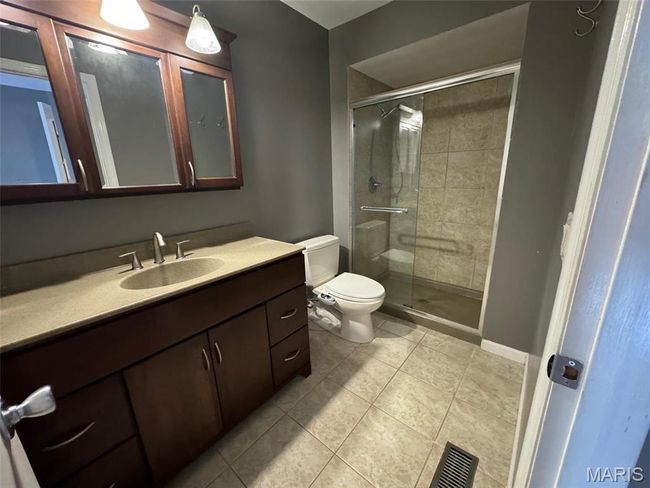 primary bathroom featuring tile patterned flooring, vanity, toilet, and a shower with shower door | Image 22