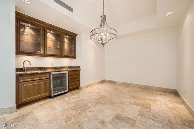 Indoor wet bar featuring beverage cooler, stone tile flooring, baseboards, hanging light fixtures, and a chandelier | Image 10
