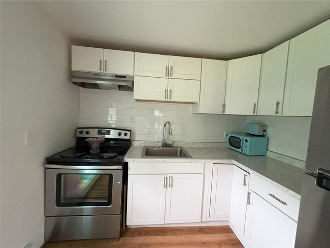 Kitchen featuring a sink, under cabinet range hood, stainless steel appliances, decorative backsplash, and light wood-style floors | Image 4