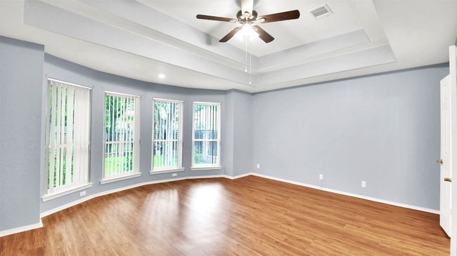 Master bedroom with vinyl plank floors, ceiling fan, and a tray ceiling | Image 26