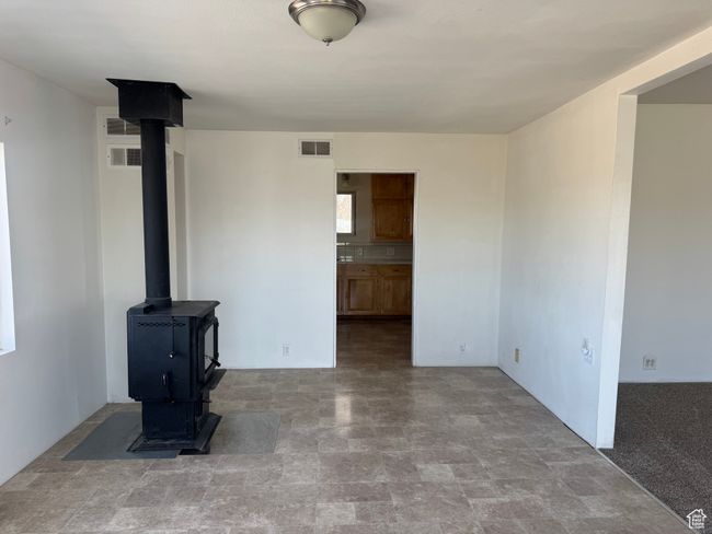 Unfurnished living room featuring stone finish flooring, a wood stove, and visible vents | Image 28