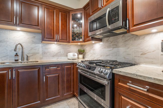 Kitchen with stainless steel appliances, a sink, decorative backsplash, light stone countertops, and glass insert cabinets | Image 14