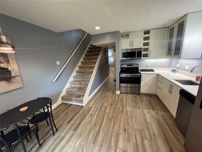 Kitchen with stainless steel appliances, a sink, light wood-style flooring, open shelves, and glass insert cabinets | Image 7