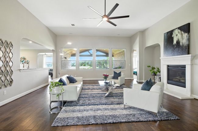 Living room with ceiling fan, arched walkways, a glass covered fireplace, and wood finished floors | Image 6