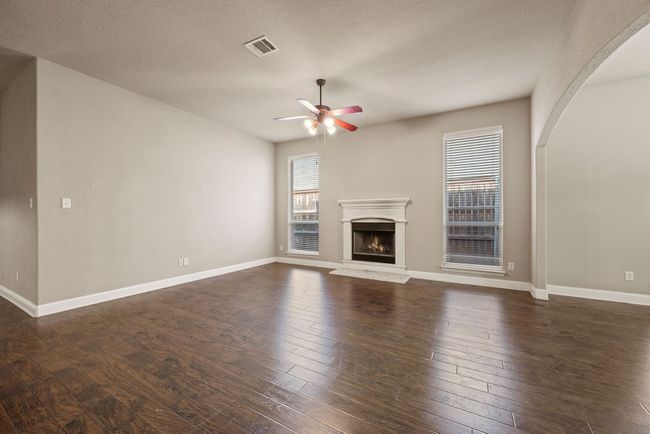 Unfurnished living room featuring a warm lit fireplace, a ceiling fan, dark wood-style flooring, and visible vents | Image 8