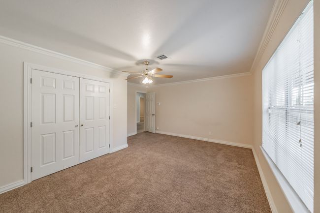 Large downstairs bedroom featuring ceiling fan, carpet floors, crown molding, and a closet | Image 12