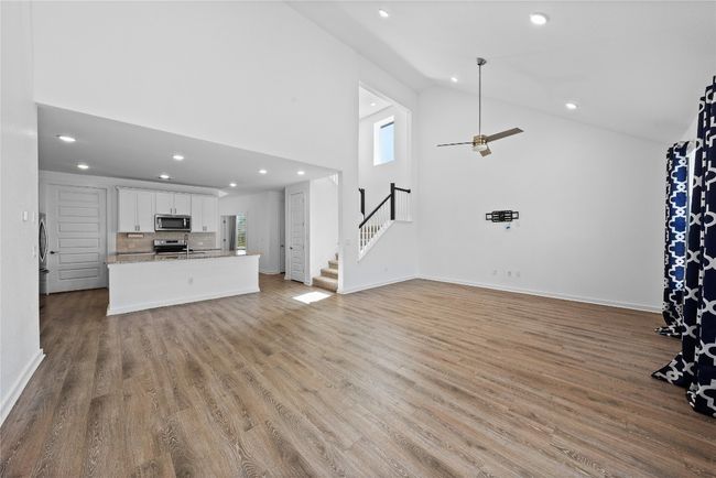 Unfurnished living room with high vaulted ceiling, light wood-style flooring, stairway, and plenty of natural light | Image 11