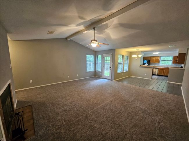 Unfurnished living room featuring baseboards, visible vents, ceiling fan with notable chandelier, dark carpet, and vaulted ceiling with beams | Image 8