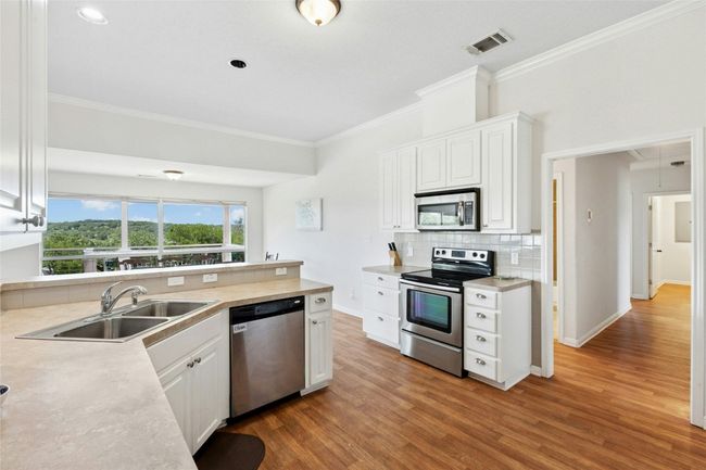 Kitchen with stainless steel appliances, crown molding, decorative backsplash, white cabinetry, and wood finished floors | Image 11