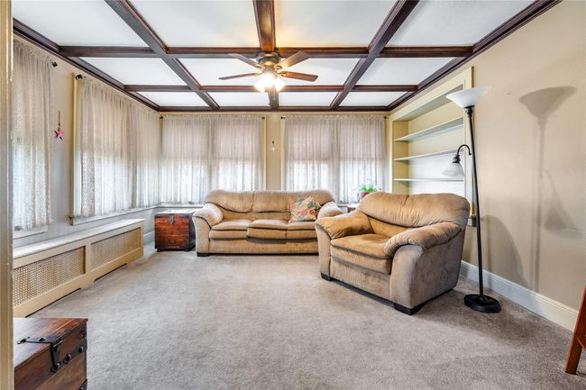Carpeted living room with radiator heating unit, coffered ceiling, baseboards, built in features, and ceiling fan | Image 17
