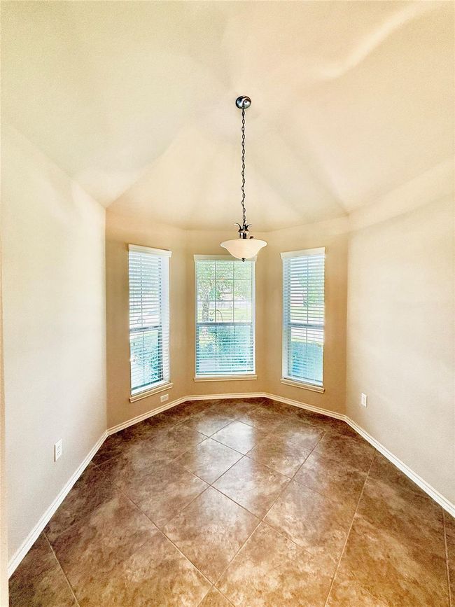 Bright, spacious kitchen den with vaulted ceilings, neutral walls, and tile flooring. It features ample natural light from large windows. | Image 4