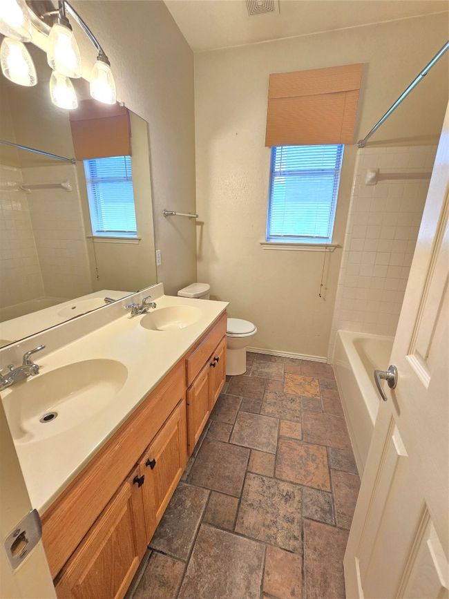 Bathroom featuring plenty of natural light, double vanity, stone finish flooring, and tub / shower combination | Image 6