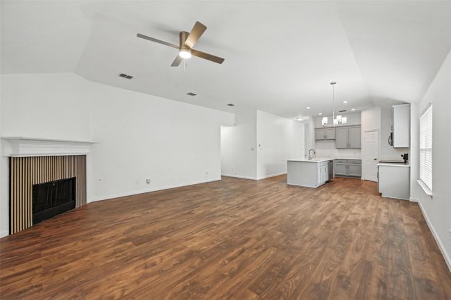 Unfurnished living room featuring vaulted ceiling, a sink, ceiling fan, a fireplace, and dark wood-style flooring | Image 18