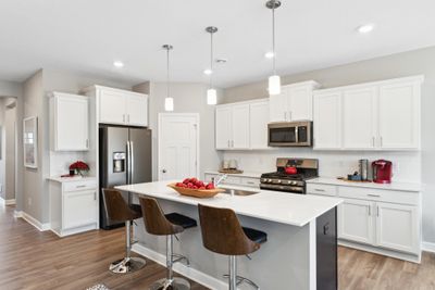 (Photo of decorated model, finishes will vary) One-level living with dream kitchen featuring an oversized island, quartz countertops, tile backsplash, slate finish appliance package including refrigerator and walk-in pantry. | Image 1