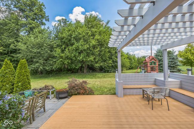 deck with a fire pit, a playground, a lawn, a pergola, and view of wooded area | Image 33