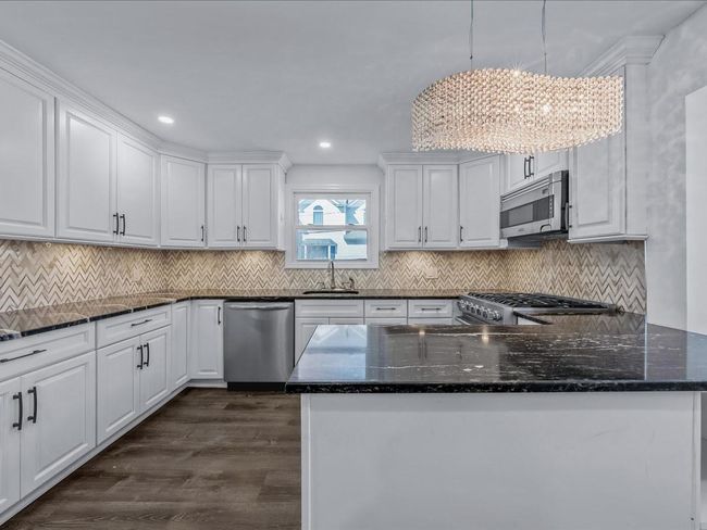 Kitchen featuring stainless steel appliances, a sink, white cabinets, dark wood-type flooring, and dark stone countertops | Image 5