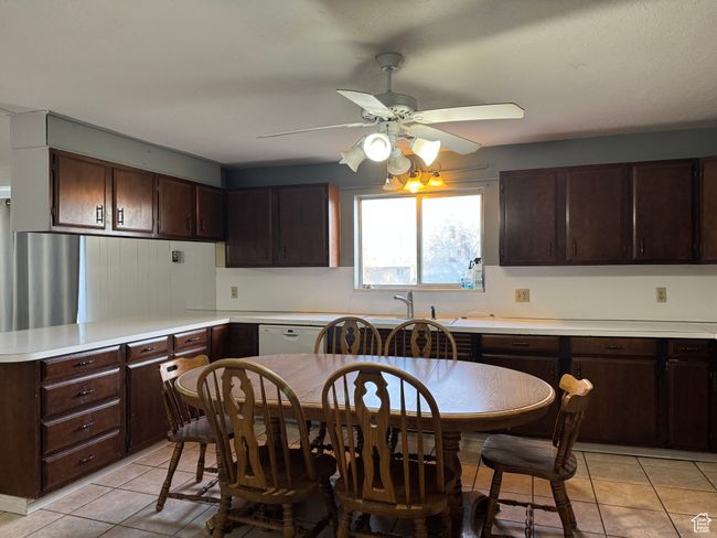 Kitchen with a ceiling fan, dark brown cabinetry, light tile patterned floors, light countertops, and a sink | Image 7