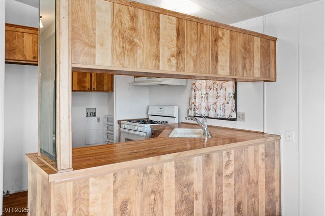 Kitchen with under cabinet range hood, white gas range, brown cabinetry, and a sink | Image 11