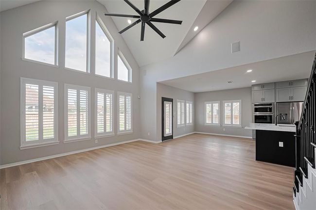 Spacious living area features high vaulted ceilings, large windows with shutters for abundant natural light, and an open floor plan leading to a modern kitchen with stainless steel appliances | Image 6